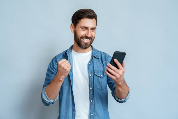 istock Man looking at mobile phone screen gesturing yes with clenched fist over blue 1347959461
