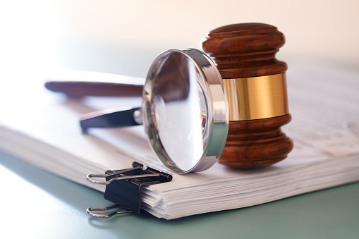 A gavel and a magnifying glass on top of a stack of legal documents. Photographed with a very shallow depth of field.