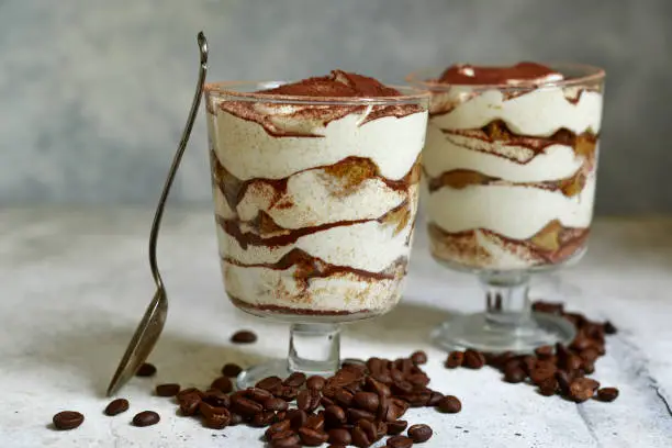 Tiramisu - traditional italian dessert with mascarpone and bisquit in a glasses on a light slate, stone or concrete background.