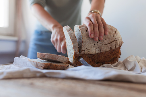 Close-up of a female hand taking a knife and slicing homemade loaf of bread