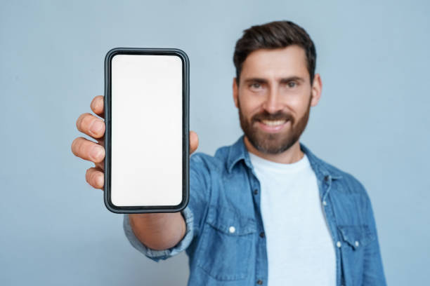 istock Satisfied smiling man showing mobile phone blank white screen mockup to camera 1347964507