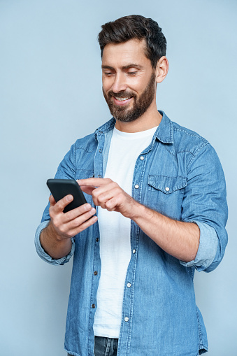 Portrait of handsome macho guy perfect appearance neat hairstyle easy-going person holding browsing telephone wear specs casual denim outfit isolated blue studio background copy space