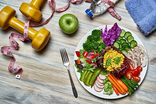 Top view of a colorful spring salad on rustic white wood table. Included ingredients tomatoes, broccoli, lettuce, bell peppers, mushroom, carrots, radicchio, almonds.
