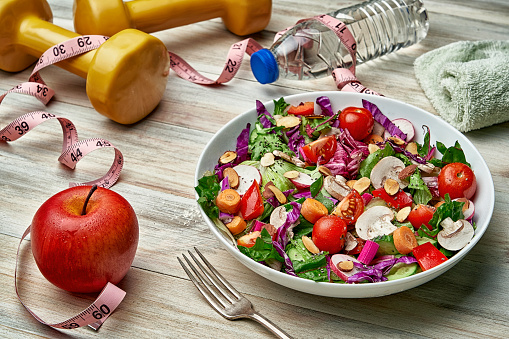 Healthy eating and diet concepts. Top view of a colorful spring salad on rustic white wood table. Included ingredients tomatoes, broccoli, lettuce, bell peppers, mushroom, carrots, radicchio, almonds.