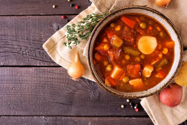 Homemade beef vegetable soup. Top down view table scene on a dark wood background with copy space.