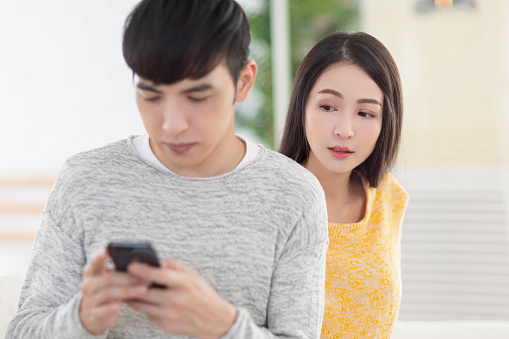 Young man using smartphone.Young woman peeks at man's smartphone screen.
