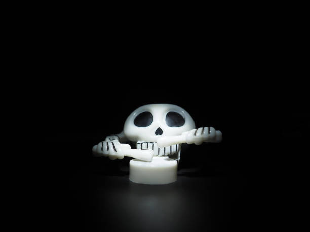 istock Skull with drumsticks and drum. Terrible clockwork toy. The skeleton is made of the skull, bones, hands and fingers. Black background. Halloween and horror theme. White skull with black eye sockets 1347976484