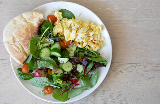 Top view of a plate with Scrambled and fresh vegetable salad with Pita bread.