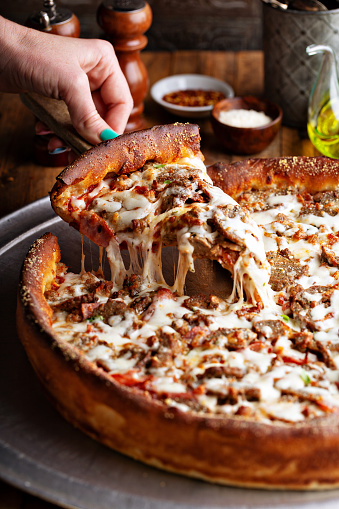 Deep dish meat pizza on a wooden table with a slice being pulled