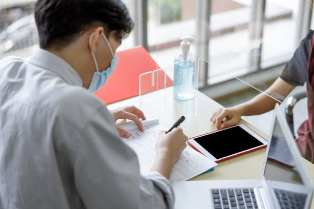 istock business man workers wearing face mask and clear shield having discussion through glass partition at the office as part of business in new normal during the outbreak of COVID-19 or Coronavirus 1347988286