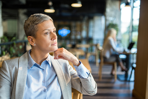 Portrait of businesswoman contemplating while relaxing in coffee shop. Beautiful elegant woman thinking of new ideas while sitting in cafeteria.
