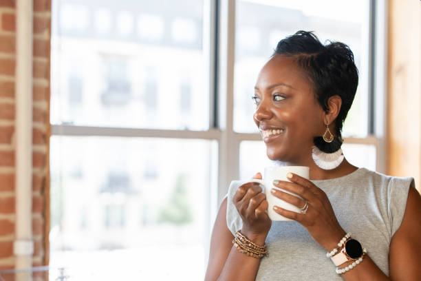 istock Woman holding coffee mug and smiling while looking out window 1347998240
