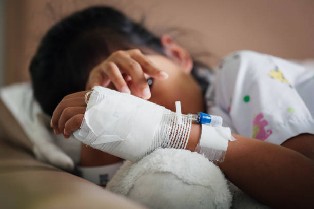 Sick kid feeling unwell lying down and hugging her doll in the bed while stay in private patient rooms in the hospital. stock photo