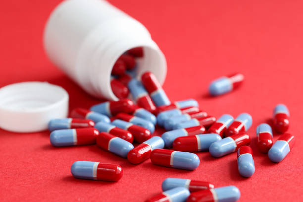 istock Blue-red medical pills scattered from jar lie on a red background 1348004597