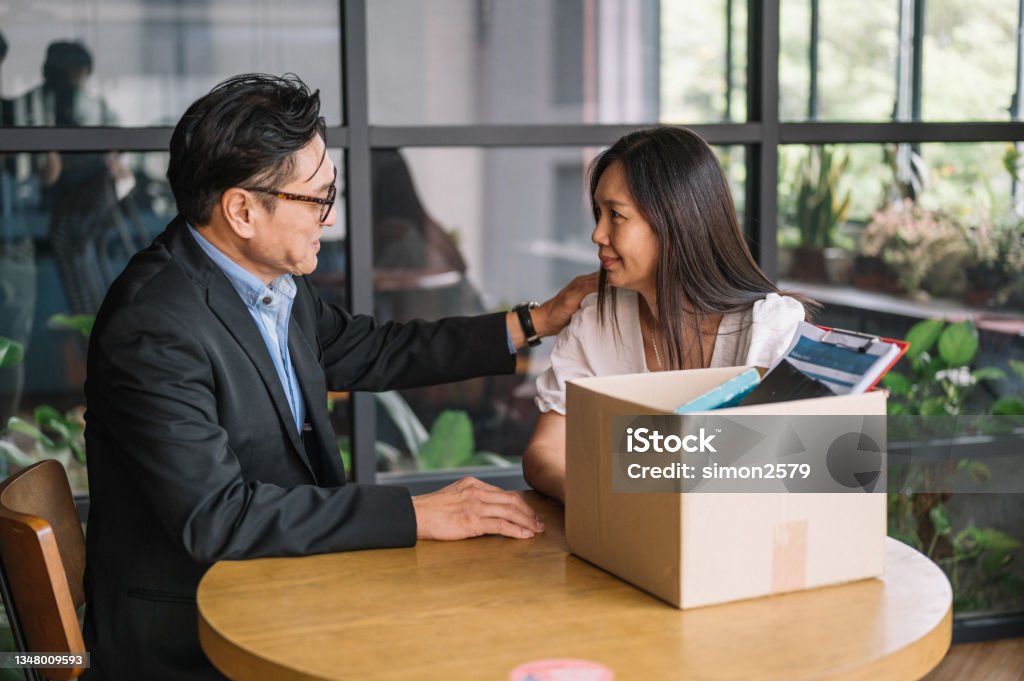 Employee packing box at workplace on last working day Frustrated upset Asian female office worker packing her belongings stuff in a cardboard box feels unhappy stressed about dismissal and losing job. Asian man colleague sympathy for a colleague who was fired. Leaving Stock Photo