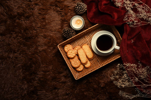 Above view aroma candle, wooden tray with coffee cup and cookies on fluffy carpet.