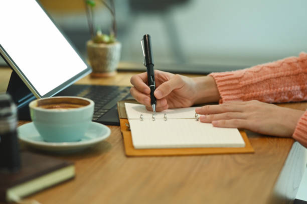 istock Woman sitting in front of computer tablet and writing information on notebook. 1348012296