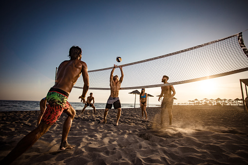 Young friends having fun while playing beach volleyball at sunset. Copy space.