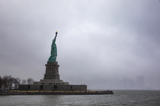 Side View of Statue of Liberty composite with a foggy covered the New York City in the background