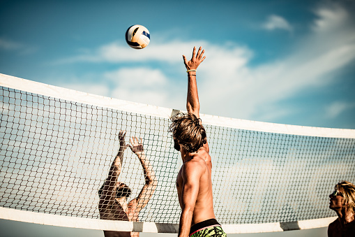 Young male friends having fun while playing volleyball on the beach.