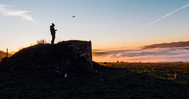 homem em pé em uma colina fotografando com seu drone no alto da montanha - drone subindo - fotografias e filmes do acervo