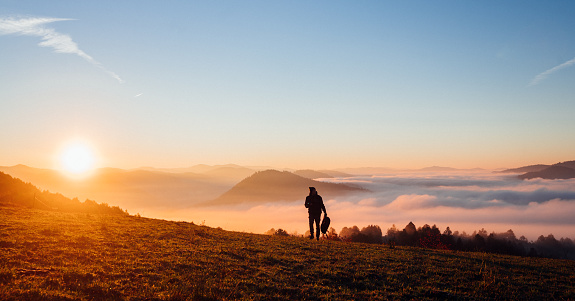 Aerial view of a dreamy landscape picture of a man standing on top of a hill in foggy mountains at sunrise