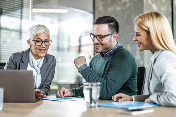 szczęśliwy starszy agent korzystający z komputera z młodą parą w biurze. - senior adult retirement financial advisor finance zdjęcia i obrazy z banku zdjęć