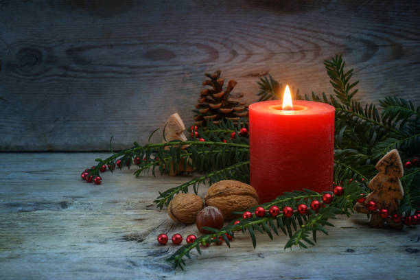 istock Warm light on a cold winter night from a red candle with flame, evergreen yew branches, nuts and Christmas decoration on blue gray rustic wooden planks, copy space, selected focus 1348018559
