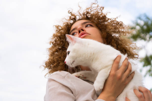A beautiful teenage girl with curly hair holds a white cat close to her face. She is enjoying time with her pet.