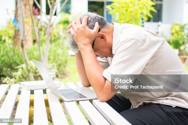 Portrait Of An Old Elderly Asian Man Holds The Head With His Hand Cause Of Stress After Try To Use A Computer Laptop In The Backyard After Retired Concept Of Ageism And Hobbies After Retirement Stock Photo - Download Image Now