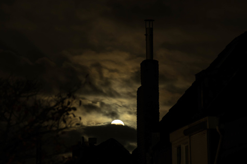 Full moon in silhouette with chimney twigs and leaves