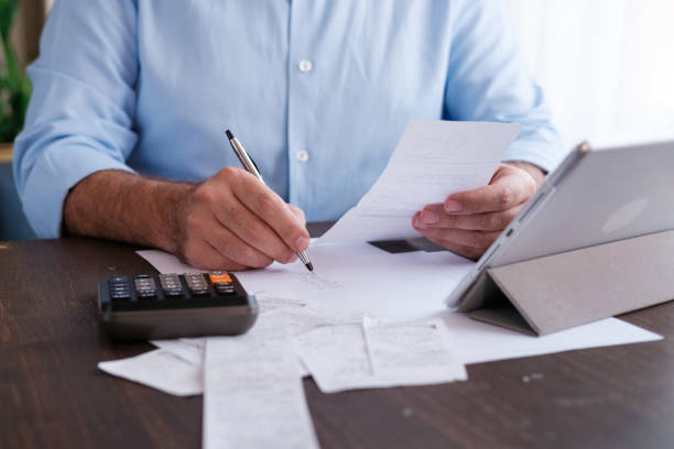 man calculating personal expenses at home - tax tax form financial advisor calculator imagens e fotografias de stock