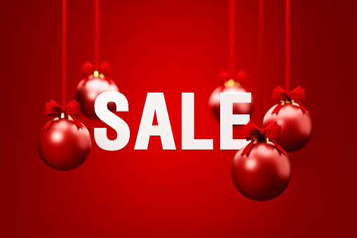 Sale and red Christmas baubles hanging over red background. Christmas and festivity concept. Horizontal composition with selective focus and copy space.
