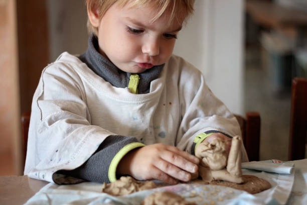 Cute little kid playing with modeling clay in pottery workshop, craft and clay art, child creative activities, education in Arts