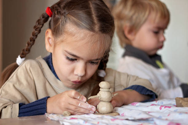 Cute little kid playing with modeling clay in pottery workshop, craft and clay art, child creative activities, education in Arts