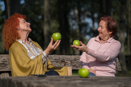 Close up of two female seniors eating fruit at a picnic in the park.