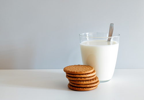 Glass of milk and six round butter biscuits on a white background.