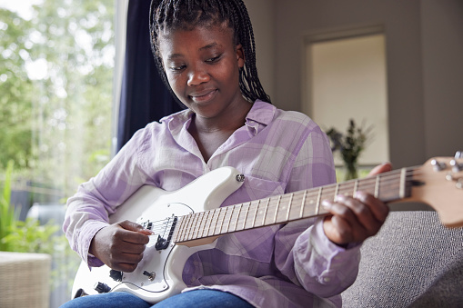 Teenage Girl At Home Learning To Play Electric Guitar