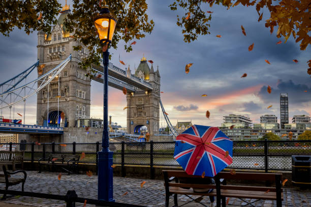 London in autumn time concept with a person holding a british umbrella sitting in front of Tower Bridge London in autumn time concept with a person holding a british flag umbrella sitting on a bench and enjoying the moody evening view to the famous Tower Bridge london stock pictures, royalty-free photos & images