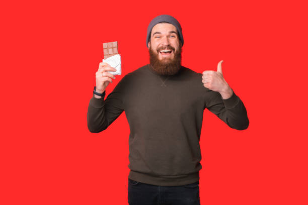 Happy bearded man is enjoying chocolate and showing like gesture at the camera. stock photo