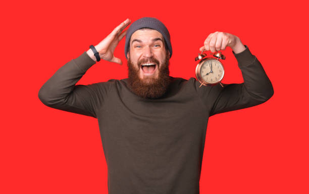 istock Bearded man is screaming loud while holding an alarm clock. 1348044102