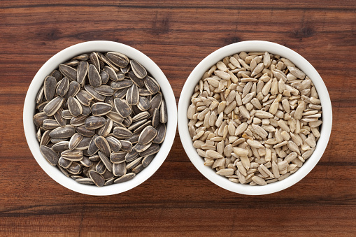 Top view of two bowls side by side with whole and peeled sunflower seeds