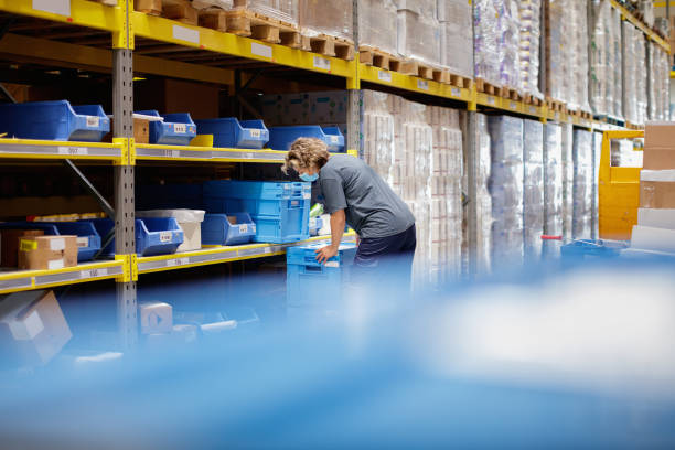 istock Warehouse worker picking up crate by the racks in storage room 1348046039