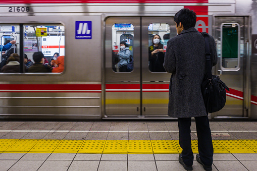 Male commuter waiting for subway train on platform in downtown Osaka, Japan.