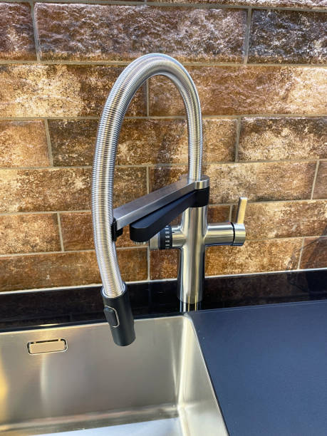 istock Close-up image of rectangular, stainless steel sink with pull out spout, single lever monobloc mixer tap, black granite countertop, brick effect tiled wall 1348050619