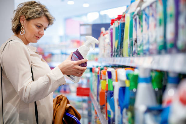 Woman choosing domestic cleaning product by the supermarket shelf Woman standing by the supermarket shelf with household hygiene products, holding cleaning agent and reading label household products stock pictures, royalty-free photos & images