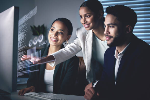 Shot of a young group of businesspeople using a computer while working in the office at night Interactive business is the future fx stock pictures, royalty-free photos & images