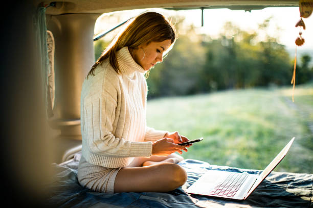 jovem usando celular e laptop na cama em camper van - telephone nature mobile phone autumn - fotografias e filmes do acervo