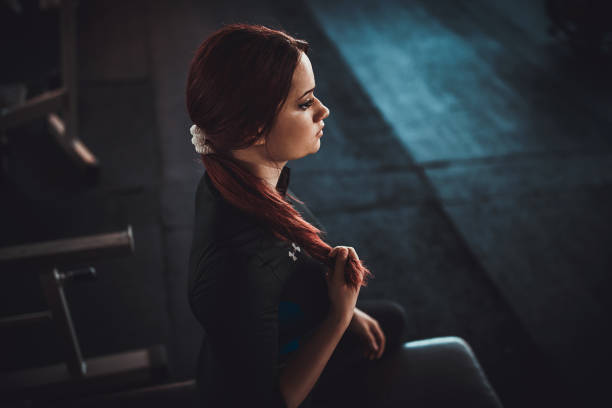 One woman, young woman sitting on weight bench in gym alone.