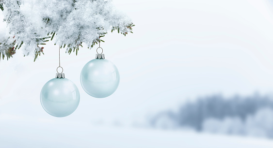 Glass Christmas balls on a fir branch against a snowy blurred background